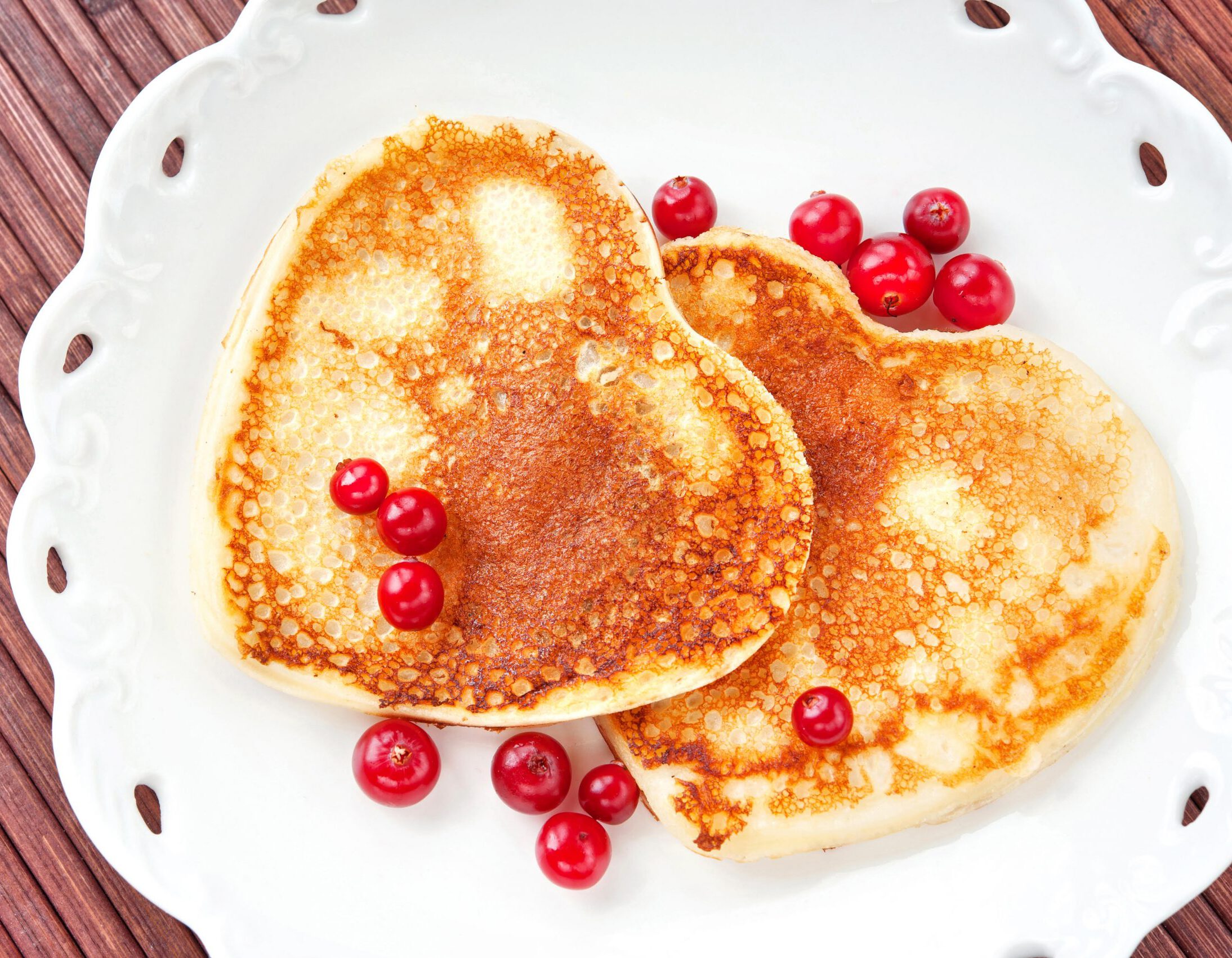 Homemade Heart shaped pancakes with cranberries on white  porcelain plate. Celebration festive dessert. Multicolored indoors closeup horizontal image